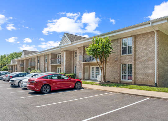 A red car is parked in a parking lot in front of a brick building.