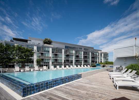 A large swimming pool with a wooden deck and lounge chairs in front of a modern building. at Dock 79, Washington, DC