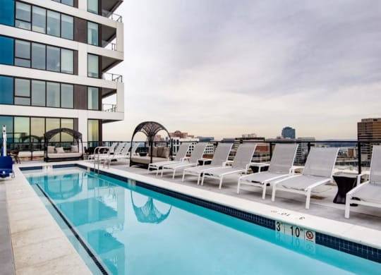 a swimming pool with white lounge chairs and a building in the background at The Boro, Tysons, VA