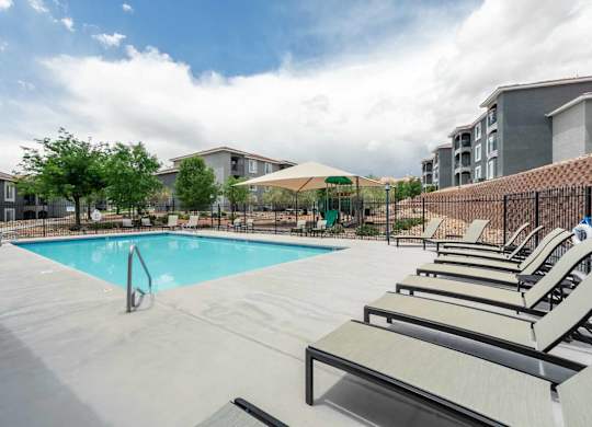 A swimming pool surrounded by sun loungers and trees at West Park Apartments, Albuquerque