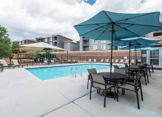 A poolside area with tables and chairs and umbrellas at West Park Apartments, Albuquerque