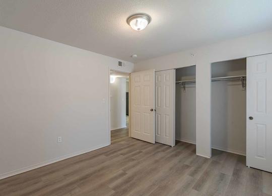 A room with a white wall and a wooden floor with a door on the left and two closets on the right at West Park Apartments, Albuquerque