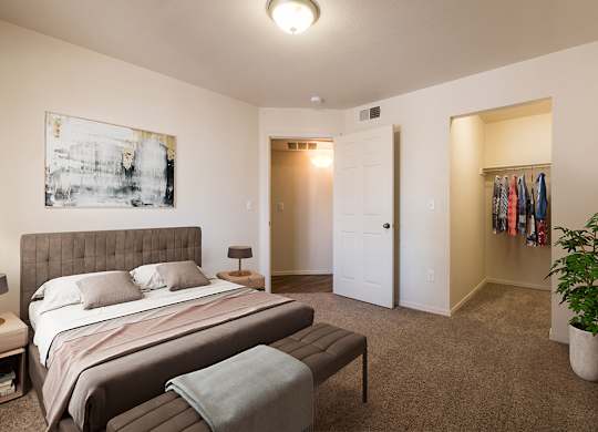 A bedroom with a bed, a bench, and a plant at West Park Apartments, Albuquerque, 87114