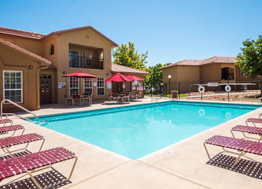 A swimming pool surrounded by red sunshades and lounge chairs at West Park Apartments, Albuquerque, NM