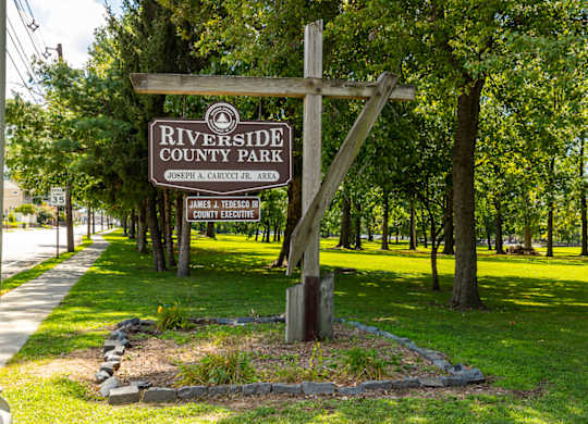 A sign for Riverside County Park is displayed in front of a wooded area at Vermella Lyndhurst apartments, Lyndhurst