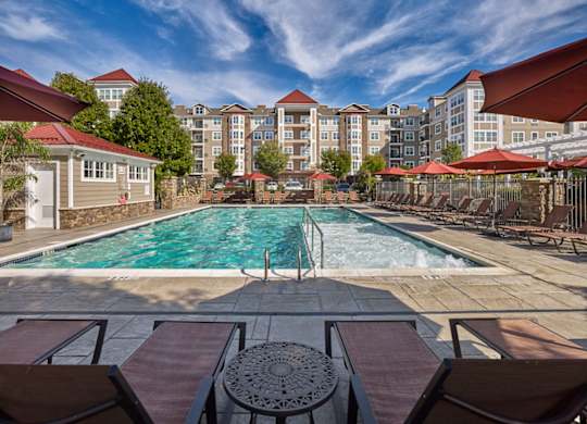 A pool surrounded by chairs and umbrellas with apartment buildings in the background at Vermella Lyndhurst apartments, Lyndhurst, New Jersey