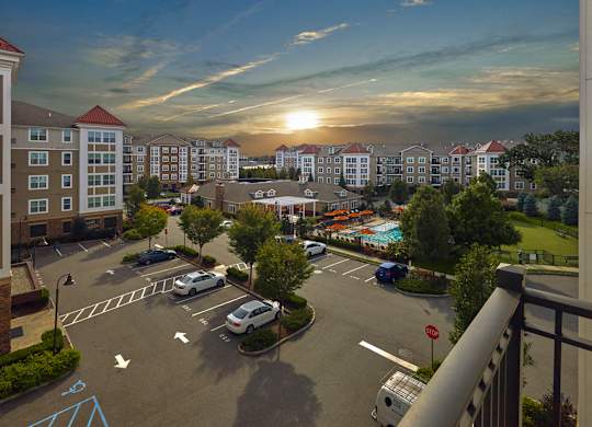 A sunset view of a parking lot with cars parked and a pool in the distance at Vermella Lyndhurst apartments, Lyndhurst, New Jersey