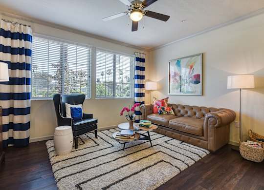 A living room with a brown leather couch, a black chair, and a striped curtain.