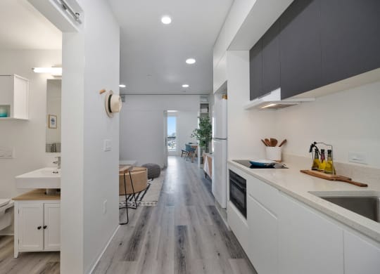 a kitchen with white cabinets and a long hallway to a living room