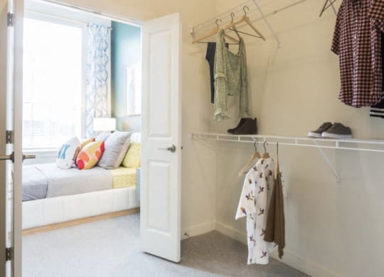a closet with clothes hanging on a rack and a door to a bedroom