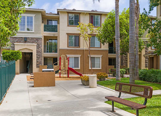 A brown bench sits on a sidewalk in front of a building.