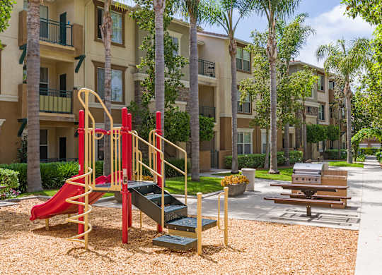 A playground with a red slide and a yellow slide in front of apartment buildings.