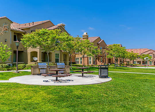 A sunny day at a park with benches and a trash bin.
