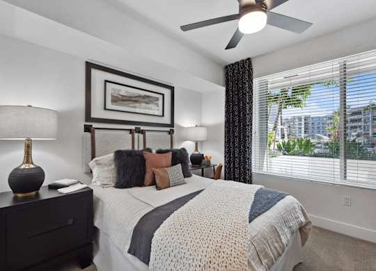 A bedroom with a large bed, a ceiling fan, and a window with blinds.