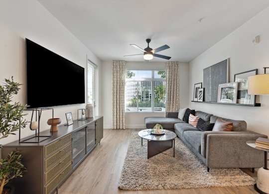 A living room with a grey couch, a black television, and a ceiling fan.