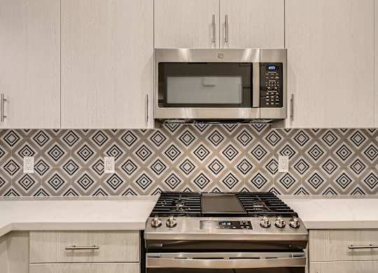 A modern kitchen with a stove, microwave, and patterned backsplash.
