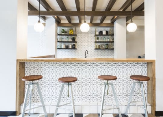a bar with three stools in front of a white tiled counter with wood