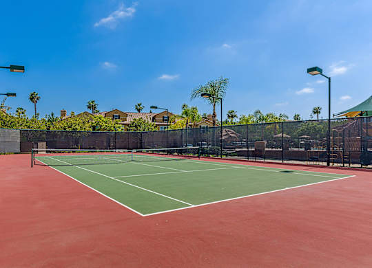 A tennis court with a red surface and green boundary lines.