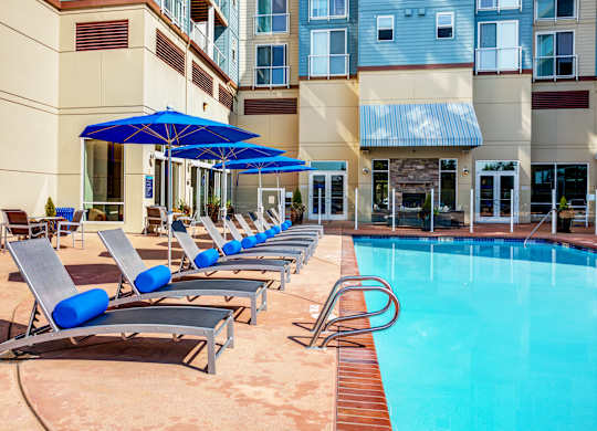 A pool with sun loungers and umbrellas in front of a building.