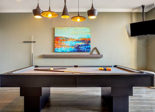 A pool table with a painting hanging above it.