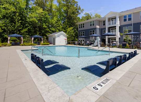A swimming pool surrounded by lounge chairs and umbrellas in front of a residential building.