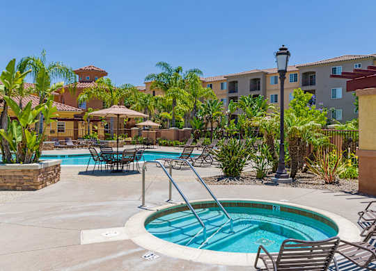 A pool surrounded by chairs and plants with a building in the background.