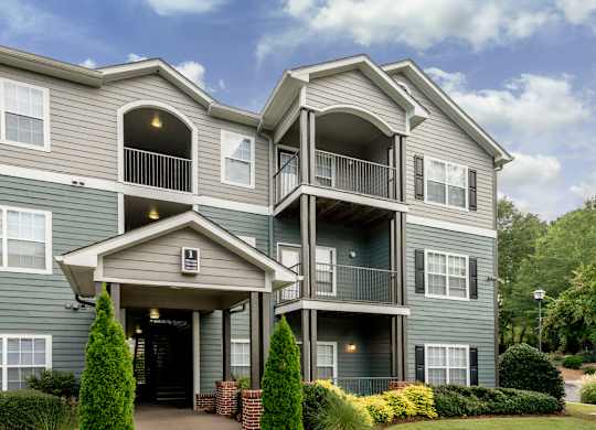 A grey two-story apartment building with a balcony on the second floor.