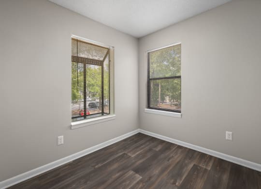 an empty room with wood floors and two windows