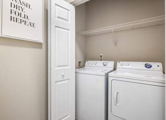 an empty laundry room with two white washers and dryers and a white door at Mariners Crossing, Raleigh