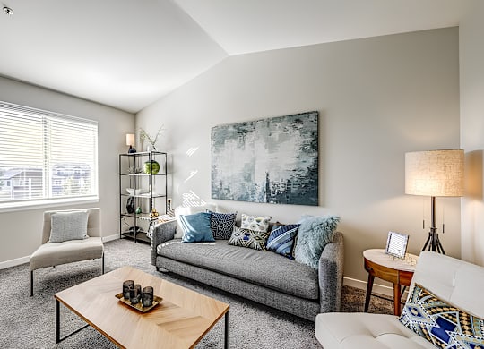 A living room with a grey couch, a wooden coffee table, and a large painting on the wall.