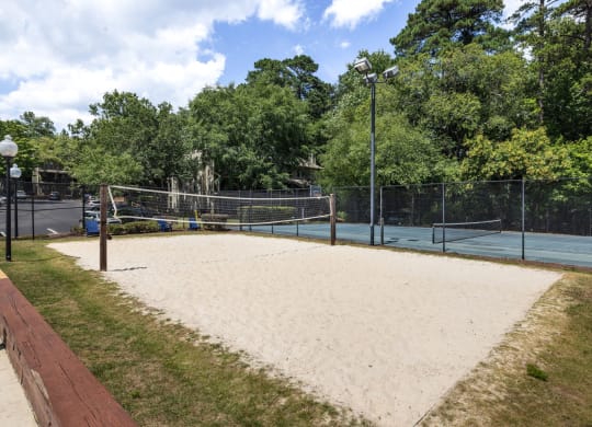 the sand volleyball court is in front of the tennis court and trees