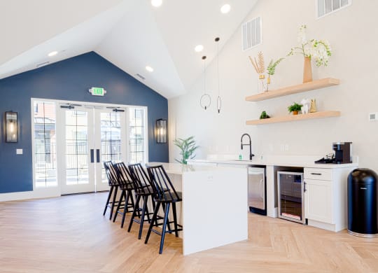 a white kitchen with a blue wall and a white island with black chairs