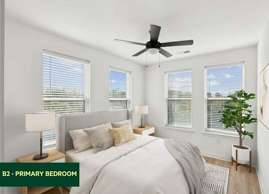 A bedroom with a bed, two lamps, a ceiling fan, and a potted plant.
