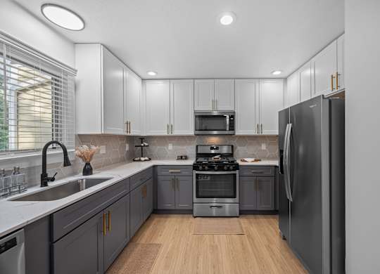 Apartments Near UNC Asheville - Verde Vista - Kitchen with Wood-Style Plank Flooring, Quartz Countertops, Two-Tone Cabinetry, Deep Sink, Range, Microwave, and Refrigerator.