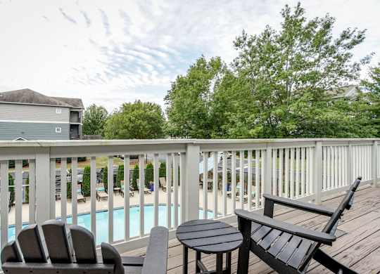 A wooden deck with a table and two chairs overlooking a pool.