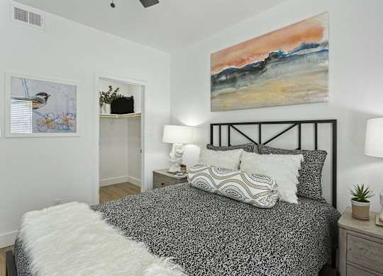 A bedroom with a bed, two lamps, and a painting on the wall.