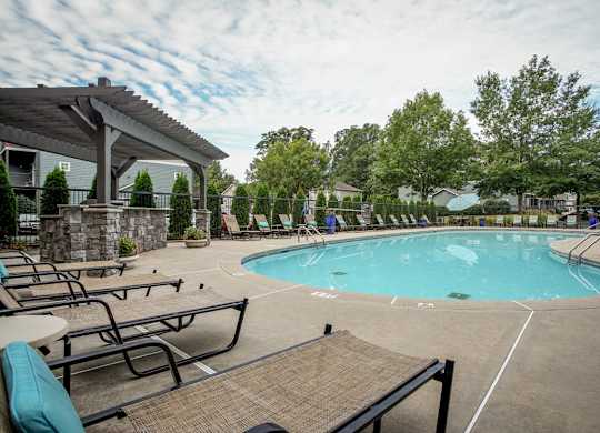 A large outdoor swimming pool surrounded by lounge chairs and trees.