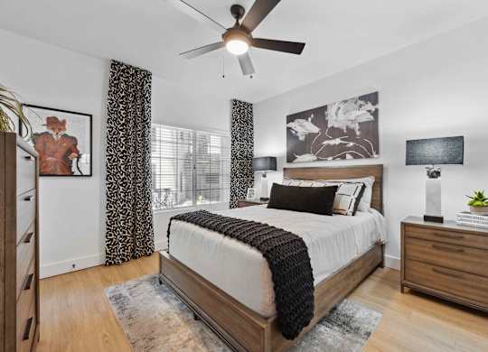 A bedroom with a bed, a ceiling fan, and a nightstand.