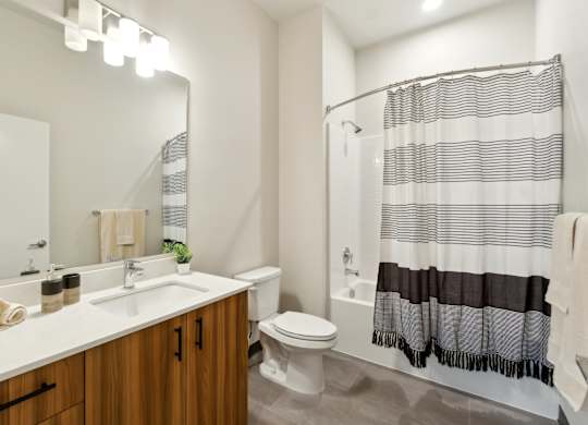 A bathroom with a white sink, a white toilet, and a shower with a black and white striped shower curtain.at Ion Town Center, Shoreline, WA
