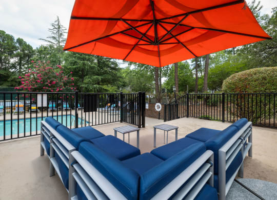 a poolside lounge area with blue couches and an orange umbrella