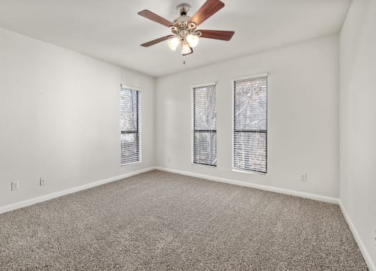 an empty living room with a ceiling fan and three windows