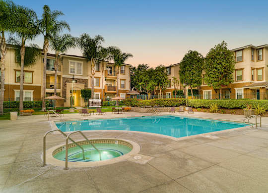 A swimming pool in a courtyard surrounded by palm trees and apartment buildings.