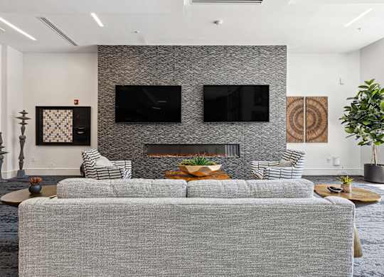 a living room with a gray couch and two televisions on the wall