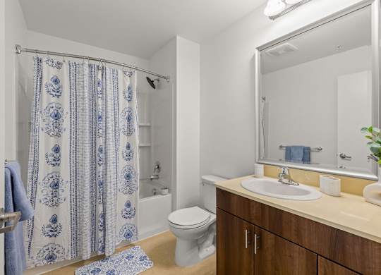 Bathroom with blue patterned shower curtain and wood vanity at Six Oaks Apartments, Bothell, 98011