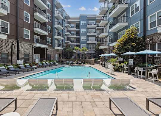 an outdoor swimming pool with lounge chairs and umbrellas in front of an apartment building