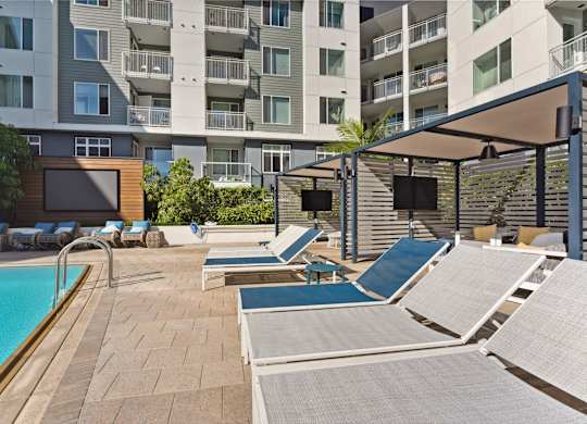 A pool area with sun loungers and a building in the background.