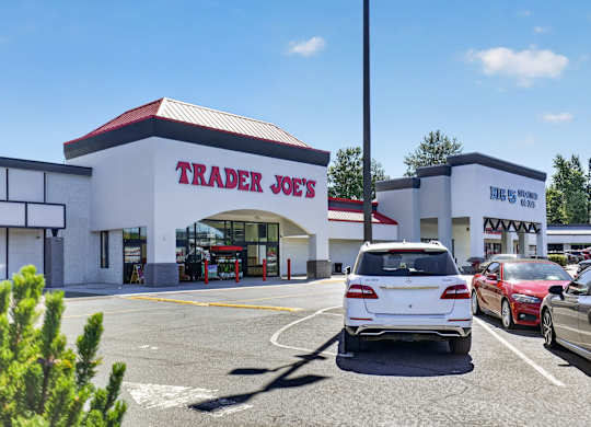 A white car is parked in front of a Trader Joe's store.