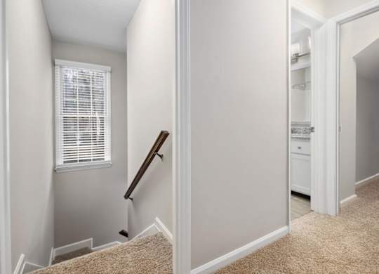 A hallway with a carpeted floor and a staircase leading to the second floor.