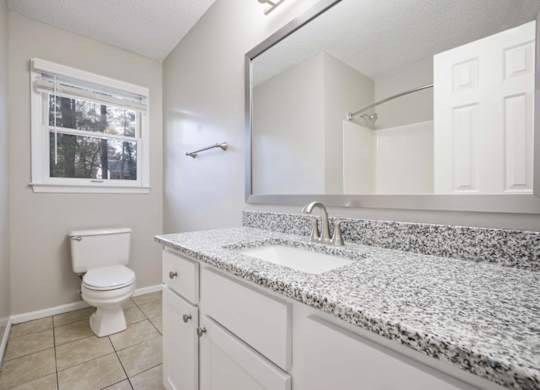 A bathroom with a granite counter top and white cabinets.