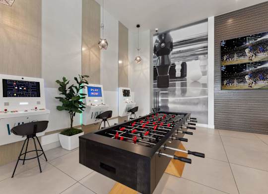 A foosball table is in the middle of a room with a wall of screens behind it.
